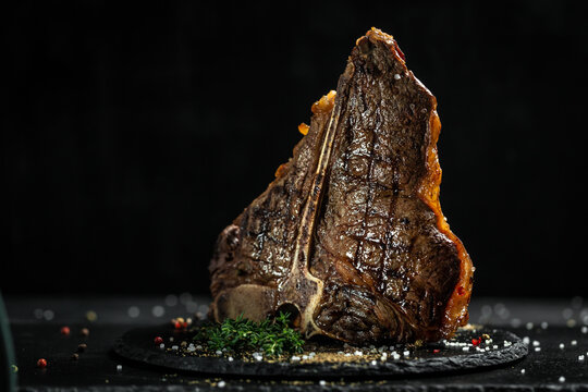 Aged Barbecue Porterhouse Steak. Beef T-Bone juicy steak rare beef with spices on a black table, banner, catering menu recipe place for text