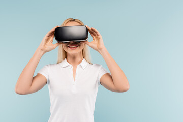 cheerful blonde woman adjusting vr headset isolated on blue