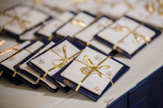  A Photo Of Small Gifts In Rows With Gold Ribbon White Paper And Blue Wrapping At Formal Affair Blurred Background