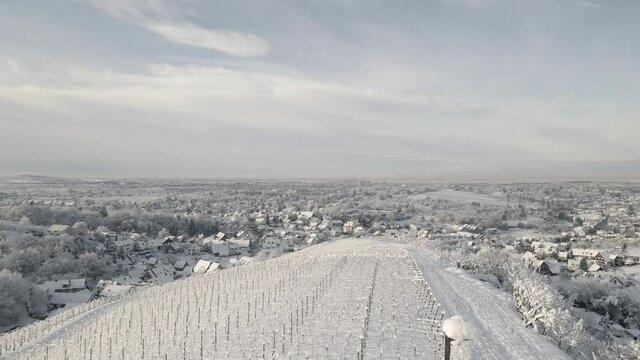 Cross Standing On Snowy Hill Overlooking Vast Vineyard Landscape During Winter In Offenburg, Germany. aerial drone