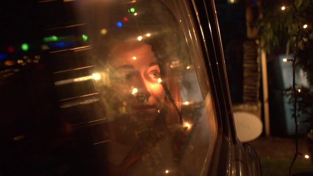 Young Woman looks out window of Black Cab with reflective Christmas lights