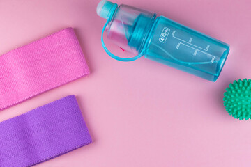 Colorful fitness gums on pink background. Elastic expanders and tapes of different color. Colored rubber and textile bands, bottle of water and massage myofascial ball. Home fitness equipment.
