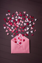 envelope with paper hearts on  grey wooden background. Hearts take off from inside open envelope. Romantic love letters.