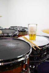 Fototapeta na wymiar Glass of light beer on professional drum set closeup. Drumsticks, drums and cymbals, at live music rock concert, in the club stage, bar, or in recording studio. White background.
