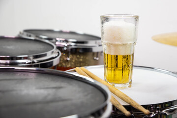 Glass of light beer on professional drum set closeup. Drumsticks, drums and cymbals, at live music rock concert, in the club stage, bar, or in recording studio. White background.