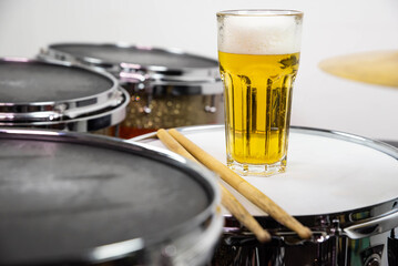 Glass of light beer on professional drum set closeup. Drumsticks, drums and cymbals, at live music rock concert, in the club stage, bar, or in recording studio. White background.