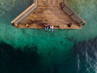 Top down aerial view. A couple are sitting on a wooden pier. Sunny day, clear water, mountain lake. The concept of romance, outdoor recreation. (Bohinjsko jezero) Slovenija. Copy space