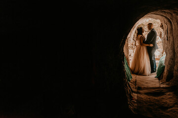 couple bride and groom wedding dress stand in a hole in rock. monastery bakota. natural tunnels rocks of Ukraine