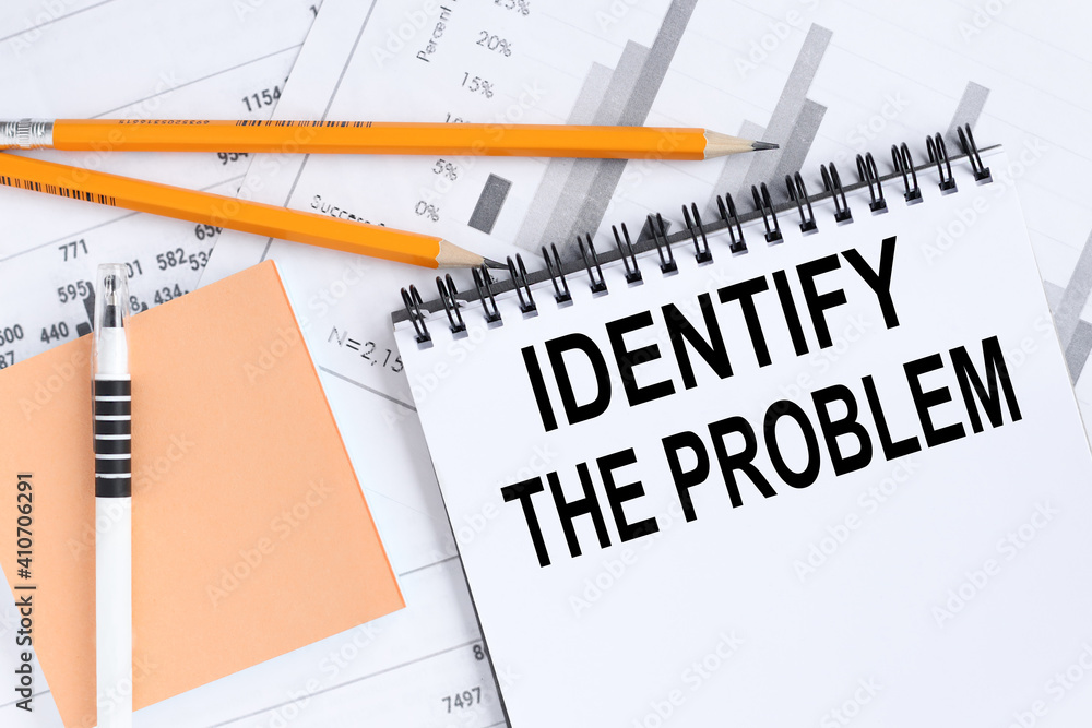 Aufkleber identify the problem, text on white notepad paper on a light background near financial charts and a 