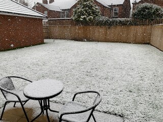 Snow still falling in a mostly empty Cheshire garden with a small round table and chairs in.
