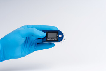 Pulse oximeter on a white background. A hand in a medical glove holds a device for health diagnostics