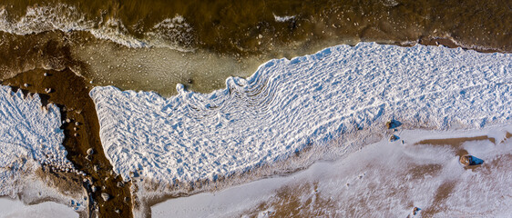 Aerial view over partialy frozen sea. White frozen waves ice texture from above shot with drone.