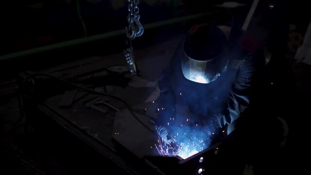 A laborious worker in a uniform and a protection mask during welding process. Clip. Welder in a workshop of a plant working with metal details.