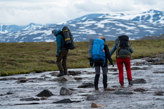 Hiking Friends Manage to wade across the river with helping hand and team work during long Hike in Padjelanta National Park, northern Europe.