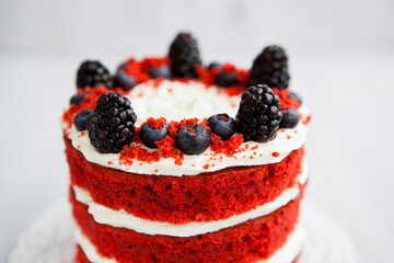 homemade red velvet cake decorated with berries on a light wooden background