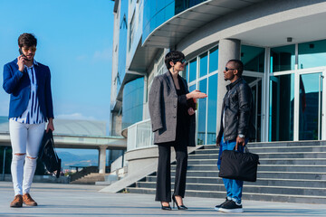 Two business colleagues discussing some reports outdoors while their young suited male colleague is talking on the phone