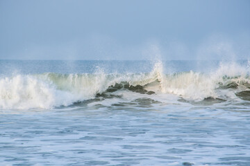 Panoramic landscape view of large foamy sea wave from Arabian Sea splashing with spray of water droplets in the air at Gokarna situated on the West Coast, Karnataka, India.