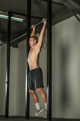 Obraz na płótnie Canvas Handsome bodybuilder doing pull-ups on horizontal bar in a indoors modern gym.