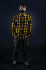 Male model with tattoos poses with hands in his pocket wearing yellow and black checkered shirt and army pants