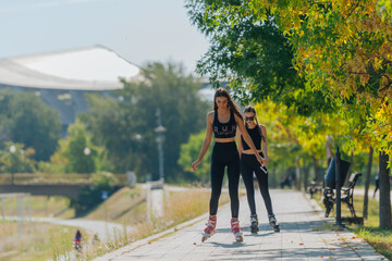 Two beautiful sportswomen roller skating in the park on a sunny day