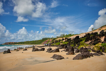Beach with volcanic rocks, sand mountains, surrounded by green plants with blue sky with clouds