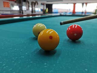 Bolas de billar a tras bandas con punta de taco, sobre mesa de paño verde, bolas roja, amarilla y blanca 