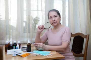 Elderly woman reading  annotation to medicines at  table