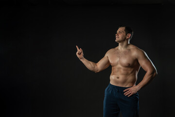 Man's hand points bare torso Young Caucasian male handsome, portrait of an isolated bodybuilder. elegance background black bodybuilder