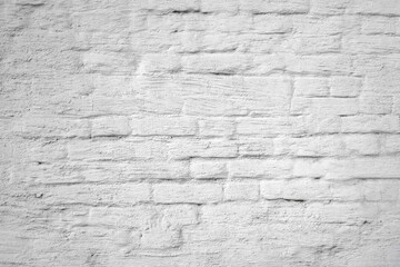 Background of the old cracked brick wall smeared with a thick layer of white paint and plaster. Close-up.