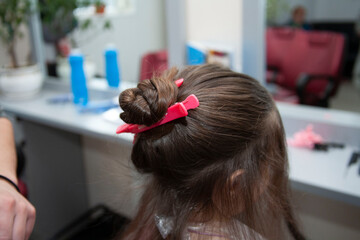 Fototapeta premium The stylist dyes the child's hair. Hairdresser and little girl in a beauty salon
