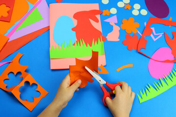 child hands makes a card, application, Easter bunny and eggs from colored paper