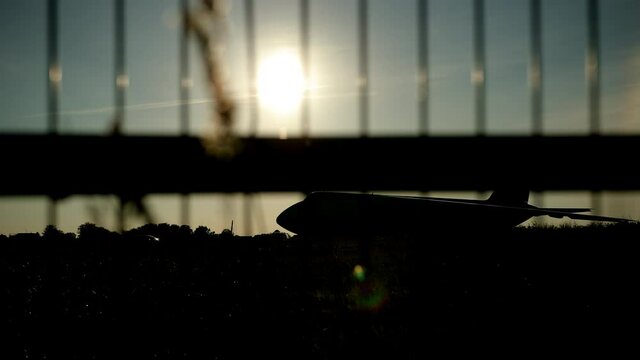 Dark silhouette of an airplane at sunset approach in the airport a beautiful sky, aircraft. In foreground is barrier grid