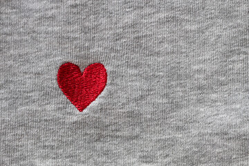 Red heart embroidered with threads on gray fabric background. Close-up, macro, copy space, flat lay. March 8, February 14, birthday, Valentine's, Mother's, Women's day celebration concept, love