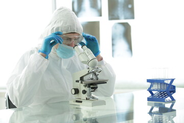 Doctor in a protective suit with gloves adjusts protective glasses near a microscope in a medical...