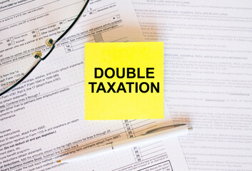 Yellow sticker with text Double Taxation on financial docs. Notepad, eyeglasses and white pen