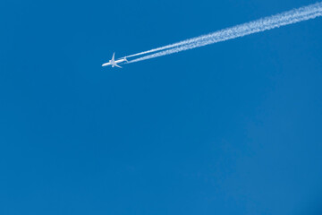 Stunning view of a commercial airplane forming contrails on a blue sky. 