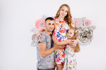 Portrait of a happy family father, pregnant mother, little daughter having fun together isolated over white with floral background