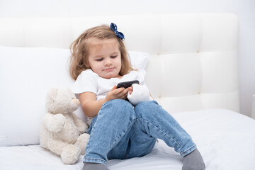 Little girl with hand in cast sitting in bed using smartphone, watching cartoon or education video