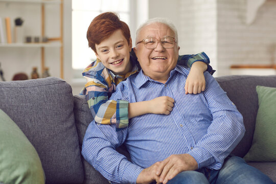 Portrait of happy old grandfather with grandson smiling and looking at camera. Senior man enjoys fun time with little grandchild at home. Love, understanding, good upbringing and family values concept