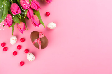 Pink easter background with pink tulips, chocolate eggs and candies. Copy space