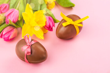 Pink easter background with pink tulips, yellow daffodils and chocolate eggs. Copy space