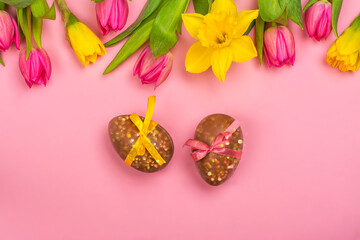 Pink easter background with pink tulips, yellow daffodils, chocolate eggs. Copy space