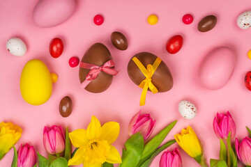 Pink easter background with pink tulips, yellow daffodils and chocolate eggs and candies. Copy space