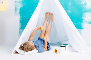 Portrait of a beautiful smiling girl with a paint roller. Little girl playing in a white wigwam on a background of colorful walls. Cheerful cute baby having fun in the nursery. baby's day. © Andriy Medvediuk