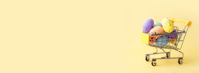 Colorful easter eggs in shopping cart on yellow background. Copy space.