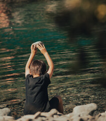 young child with black shirt throwing a stone to the lake