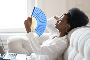 Tired Afro business woman suffering from heatstroke or hot summer flat without air-conditioner,...