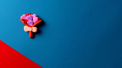 Craft from air plasticine in the form of a bouquet of hearts on a blue background with red.