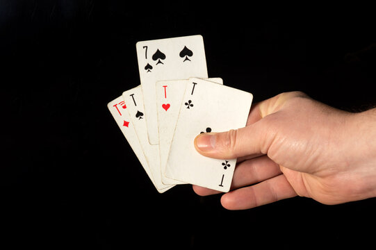 Male hands hold playing cards four aces and seven like a joker close-up on a black background