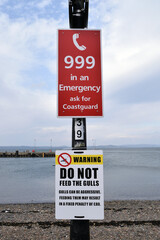 Public Signs on Steel Lamppost beside Rocky Beach with Horizon & Cloudy Sky